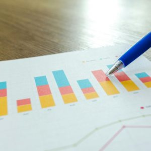 Detailed close-up of a hand pointing at colorful charts with a blue pen on wooden surface.