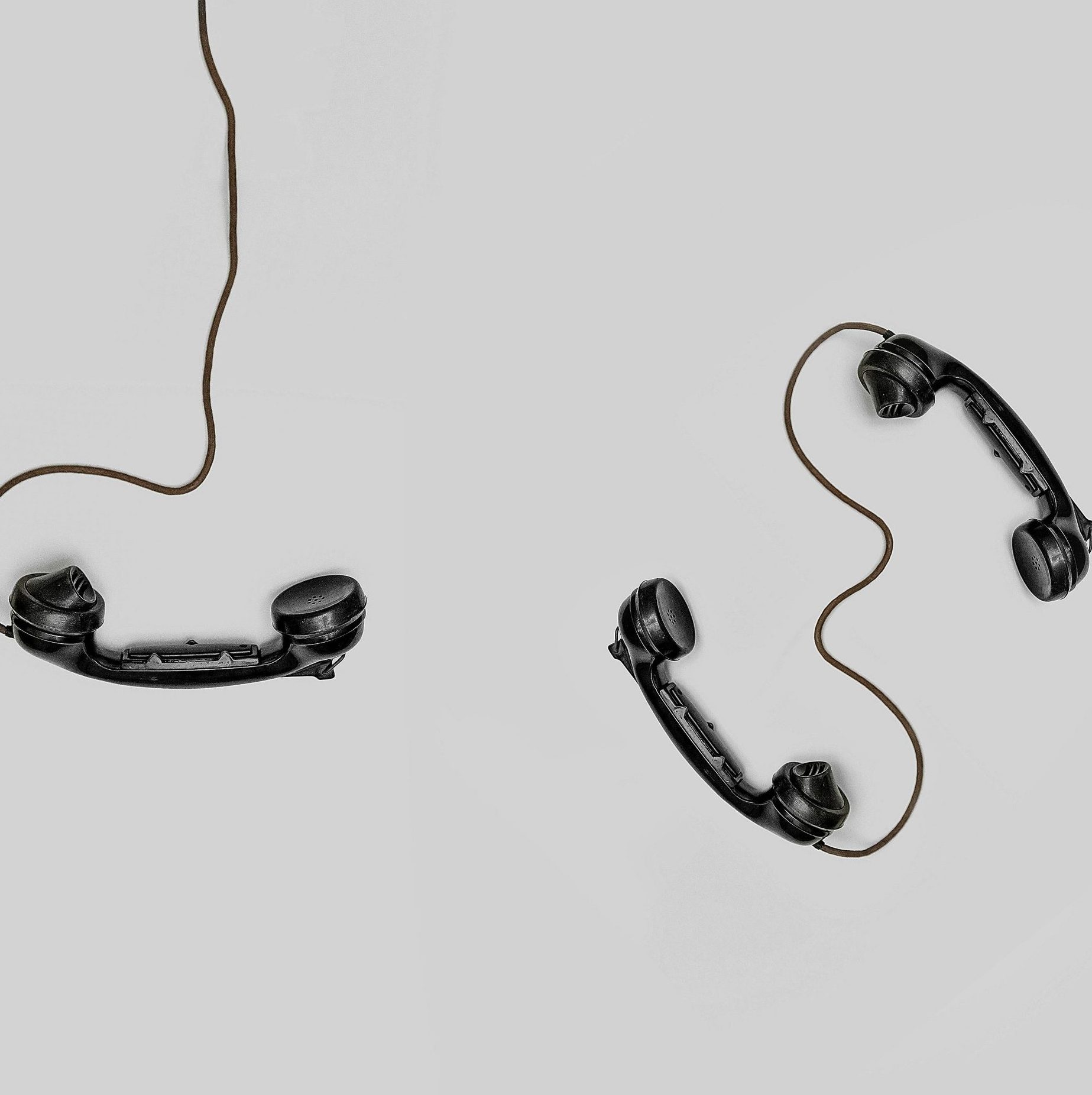 Two vintage black telephone handsets connected by cords on gray background.