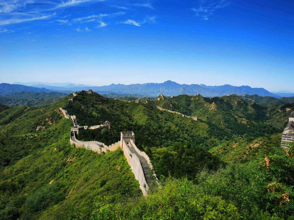 Stunning aerial view of the Great Wall of China winding over lush green hills under a clear blue sky.